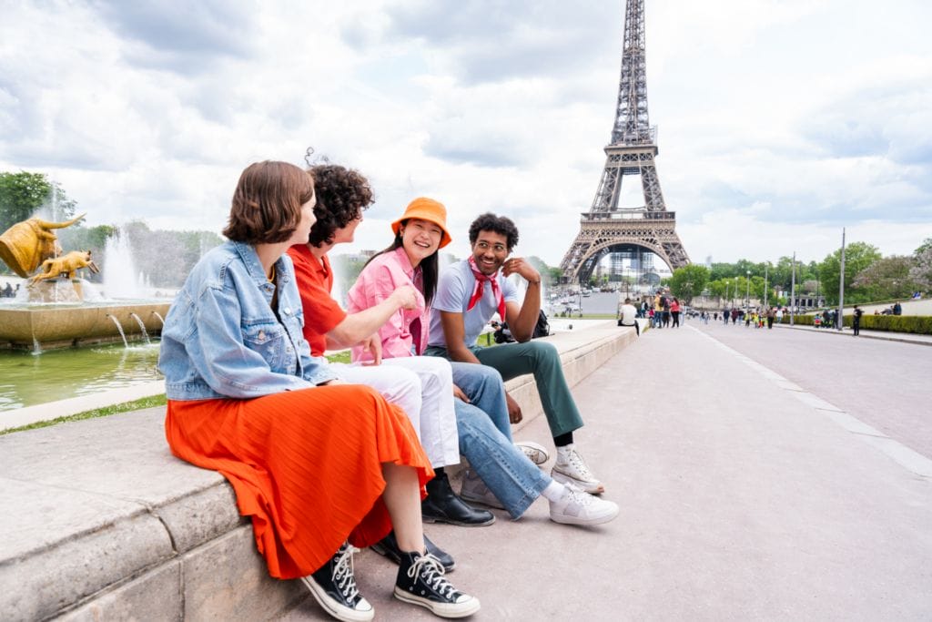 Un grupo de estudiantes entusiastas posando frente a la Torre Eiffel en París, reflejando las emocionantes experiencias y oportunidades que se abren al aprender francés.