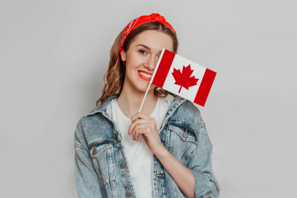 female student smiling cover half her face with small canada flag isolated white background canada day holiday confederation anniversary copy space