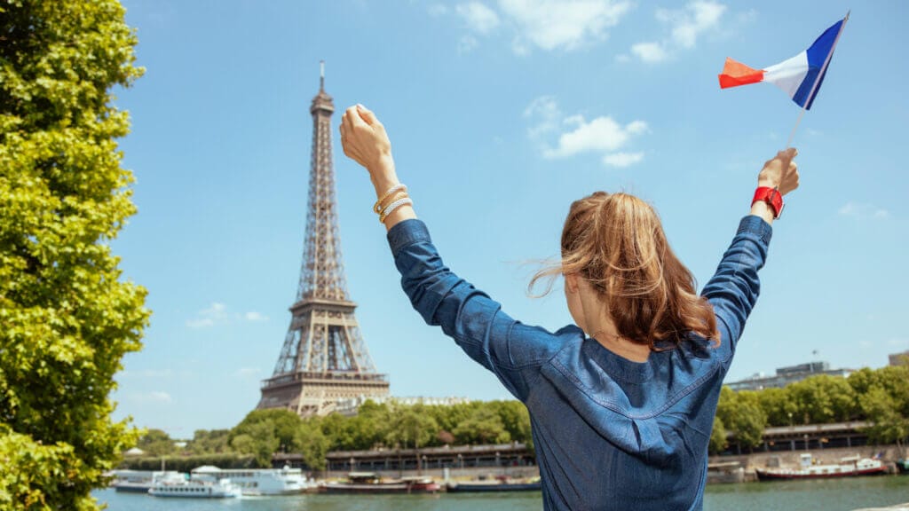 Persona viendo torre eiffel y sosteniendo bandera francesa